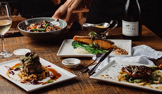 A number of fine dining dishes displayed upon a wooden table with accompanying wine